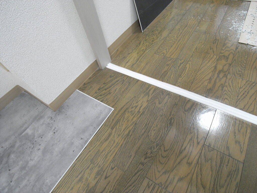 横浜市西区でフローリングの上にはめ込み式のフロアタイルを設置する工事で、敷居を外した部分には、敷居のまわりの床の動きに追従できるように、クッション材を詰めることにしました。