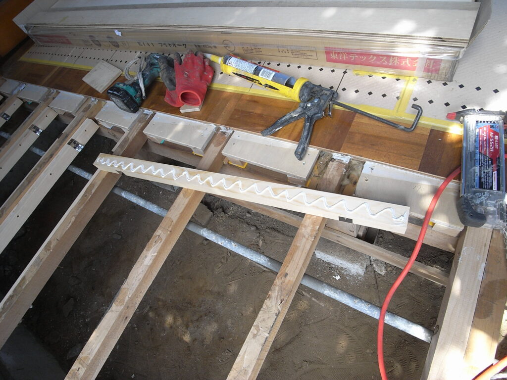 横浜市神奈川区の戸建てで下地の合板を受ける木下地を接着剤をつけて取り付けているところです。